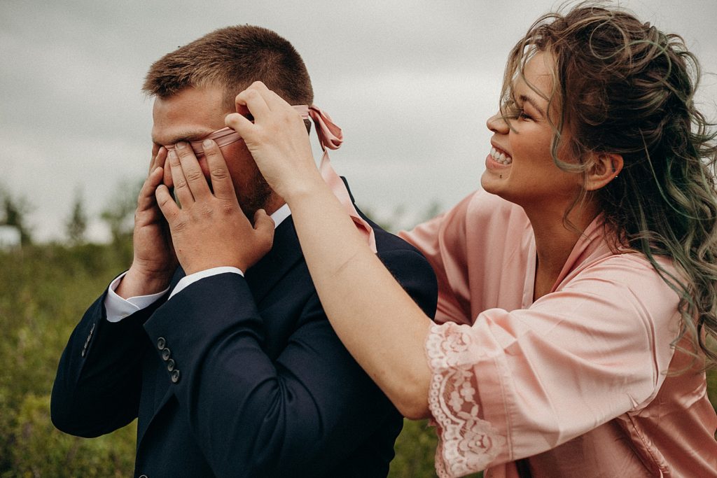Bridesmaid putting tie around Groom's eyes as blindfold for First Look